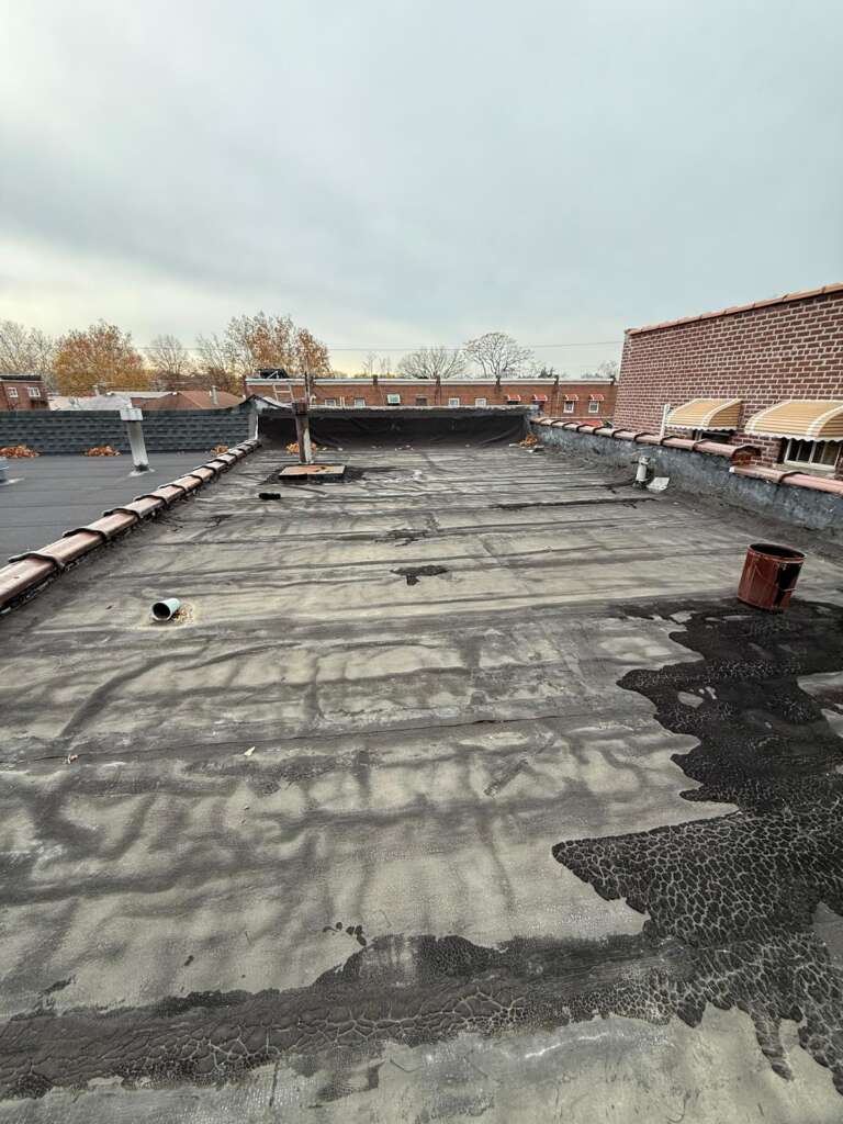 Flat roof installation in progress at Country Club, Bronx. Roofing team removing old roof, preparing deck, installing insulation and waterproof membrane for long-lasting protection