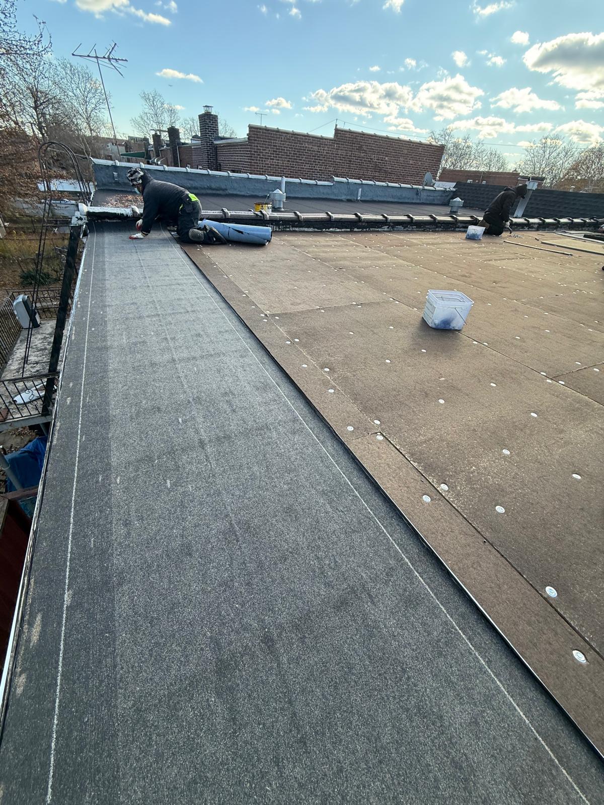 Flat roof installation in progress at Country Club, Bronx. Roofing team removing old roof, preparing deck, installing insulation and waterproof membrane for long-lasting protection